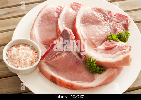 Côtelettes de porc frais sur la plaque avec du sel de roche Banque D'Images