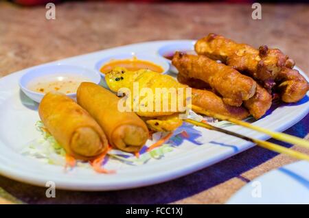 Un plat de nourriture thaï avec des rouleaux de printemps frits, en brochettes satay de poulet et de porc avec sauce chili sucrée et épicée. Aussi un c Banque D'Images