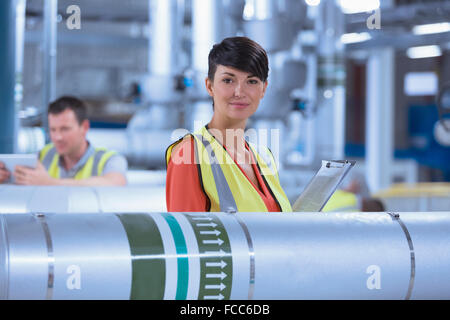 Portrait confiant travailleur féminin avec presse-papiers en usine Banque D'Images