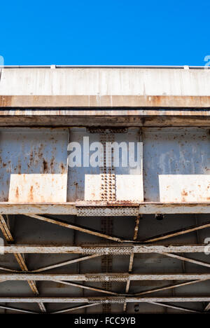 Bord du dessous de l'ancien pont d'acier rouillé et le châssis en treillis, avec des rivets rouillés et plaques, contre morceau de ciel bleu clair. Banque D'Images