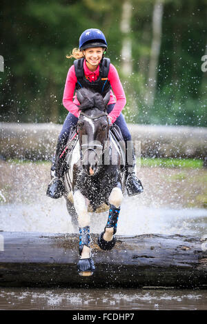 Poney Pinto. Fille sur un poney book la négociation d'un obstacle lors d'une ride. Allemagne Banque D'Images