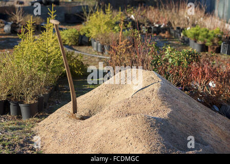 Une pelle est debout dans un tas de gravier. Plantes en pots à l'arrière-plan à l'extérieur d'une pépinière. Banque D'Images