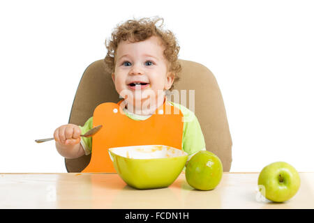 Petit enfant mange avec cuillère assis à table avec des fruits Banque D'Images