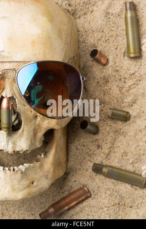 Crâne allongé dans le sable, éparpillés à la carabine et au pistolet cartouches. concept de guerre Banque D'Images