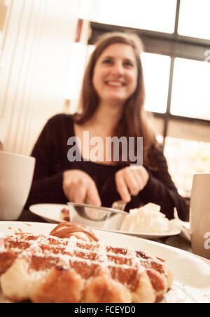 Une jolie fille brune jouit d'une gaufre de Liège au petit-déjeuner. Wannawafel, Victoria, Colombie-Britannique, Canada. Banque D'Images