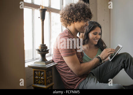 Loft vivant. Un homme et femme assise par une fenêtre à l'aide d'une tablette numérique. Banque D'Images