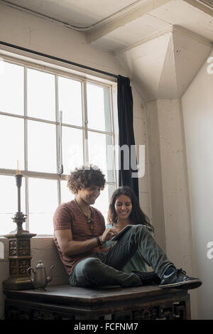 Loft vivant. Un homme et femme assise par une fenêtre à l'aide d'une tablette numérique. Banque D'Images