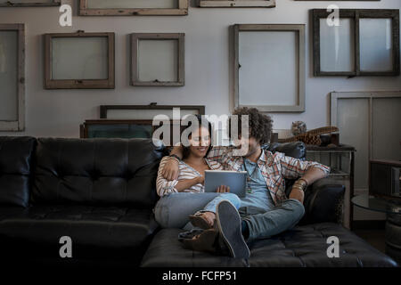 Décoration Loft. Un mur décoré de photos dans des cadres, à l'envers pour montrer le dos. Un couple sur un canapé, regardant une tablette numérique. Banque D'Images