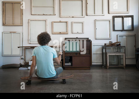 Décoration Loft. Un mur décoré de photos dans des cadres, à l'envers pour montrer le dos. Un homme assis sur une planche à roulettes à la recherche au mur. Banque D'Images