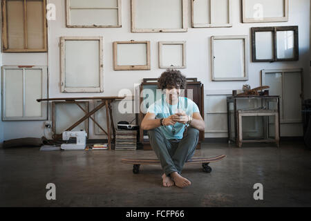 Décoration Loft. Un mur suspendu avec des cadres. Un homme assis sur une planche à roulettes contrôler son téléphone Banque D'Images