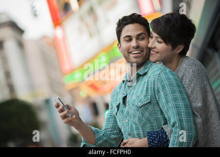 Un couple, man and woman hugging sur une rue de la ville. Homme tenant un téléphone intelligent. Banque D'Images