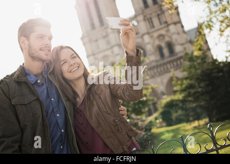 Deux personnes, un couple debout près l'un de l'autre en tenant un selfy en dehors de l'historique Cathédrale Notre Dame de Paris. Banque D'Images