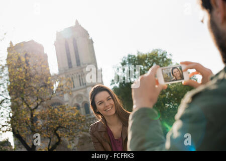 Un homme tenant un téléphone intelligent de prendre une photo d'une femme en face de la cathédrale Notre-Dame. Banque D'Images