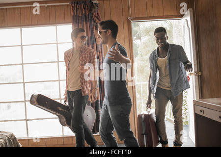 Les amis, trois jeunes hommes dans une chambre de motel, sacoches et une guitare. Banque D'Images
