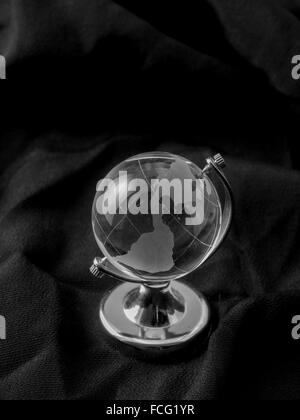 Globe en verre sur socle argent sur tissu noir. Banque D'Images