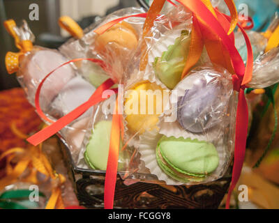 Macarons colorés dans giftwrapped plastique avec un noeud rose dans un panier. Banque D'Images