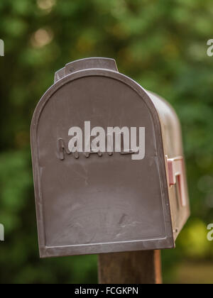 Boîte aux lettres en plastique brun avec le mot MAIL inscrit sur elle, un drapeau rouge qui est en panne, en face d'un livre vert, sur un arrière-plan flou w Banque D'Images