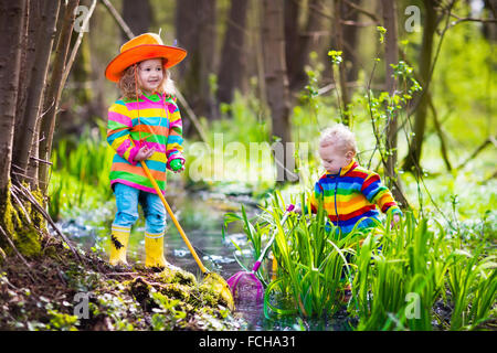 Les enfants jouent à l'extérieur. Les enfants d'âge préscolaire attraper grenouille avec filet. Garçon et fille de la pêche dans la rivière de la forêt. Banque D'Images