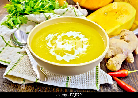 Purée de potiron avec la soupe-crème dans un bol avec une cuillère sur la serviette, persil, piment rouge gousses, graines de citrouille et potiron sur un Banque D'Images