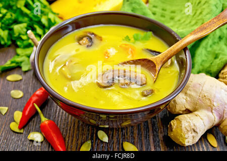 À soupe de potiron purée aux crevettes et aux champignons, une cuillère dans une tasse marron, serviette, persil, piment rouge gousses, graines de citrouille, ginger Banque D'Images