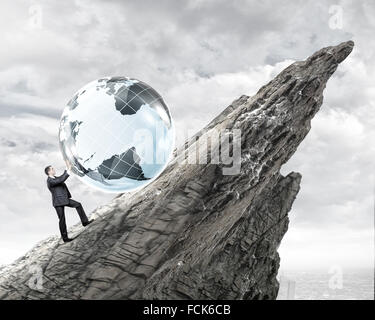 Young businessman rolling Earth planet up th hill Banque D'Images