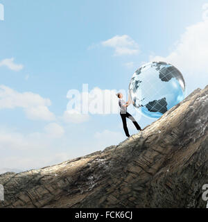 Young businesswoman rolling Earth planet up th hill Banque D'Images