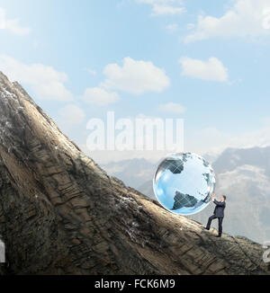 Young businessman rolling Earth planet up th hill Banque D'Images