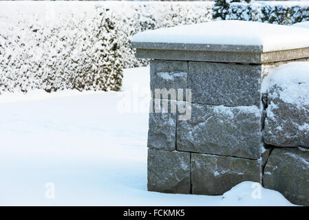 Le froid et la neige a couvert de granit gris coin d'un mur de pierre avec des arbustes Conifères couverts de neige en arrière-plan. Copier l'espace. Banque D'Images