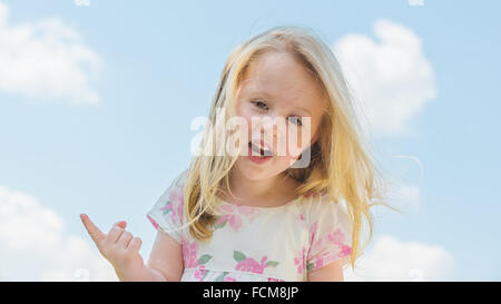 Jolie et souriante jeune fille blonde sur l'arrière-plan un ciel nuageux ciel bleu. Banque D'Images