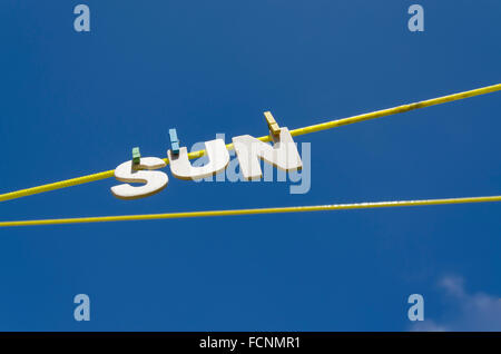 Lettres formant le mot SOLEIL suspendu à partir d'une corde à linge avec soleil en arrière-plan, image concept pour soleil ou temps ensoleillé Banque D'Images