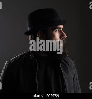 Vue de profil d'homme barbu portant hat à la route. Touche bas à haut contraste ombre sombre portrait sur fond noir Banque D'Images