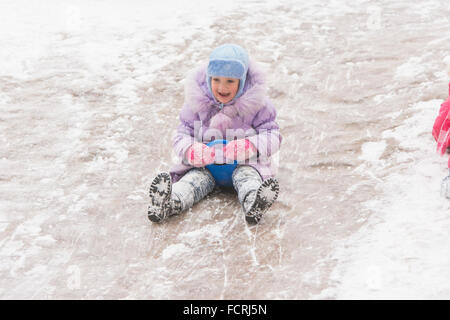 Cinq ans girl riding hiver sur une colline enneigée entourée d'autres enfants Banque D'Images