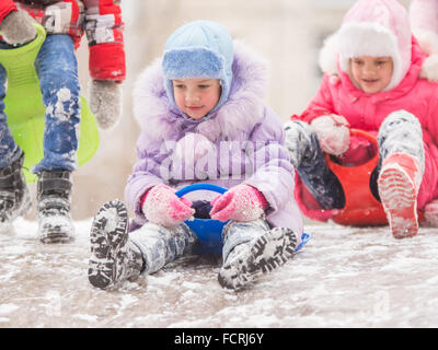 Deux jeunes filles au cours de l'hiver neige ride sur une colline entourée par d'autres enfants Banque D'Images