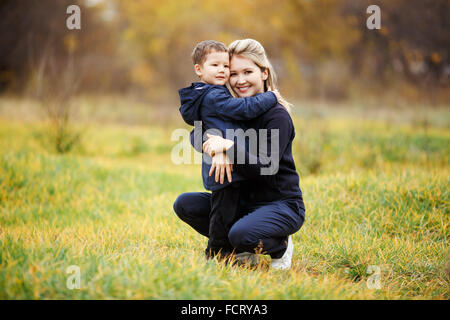 Jeune mère et son fils dans le parc forestier de l'automne, feuillage jaune. Des vêtements décontractés. Kid wearing blue Jacket. La famille incomplète, posing looking at camera de façon positive. L'enfance, les enfants dont les parents sont les meilleurs amis. Banque D'Images