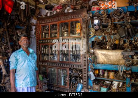 Marchand de Vente de divers Pièces de moto et scooter recyclé posant avec Display Cabinet, Kerala, Inde du Sud. Banque D'Images