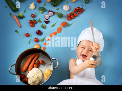 Baby Boy in chef hat avec plat de cuisson et les légumes Banque D'Images