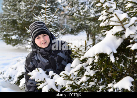 Teen boy a l'air de derrière les arbres en forêt d'hiver Banque D'Images