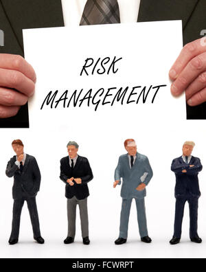 Figurine miniature Business hommes vêtus de tenues dans le message 'gestion des risques ' sur une carte étant détenu par un homme en costume Banque D'Images