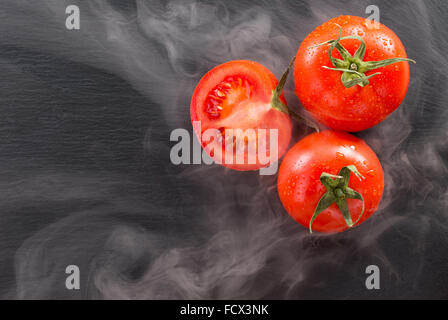 Tomates sur une pierre sombre à la lumière d'arrière-plan de la vapeur. Banque D'Images