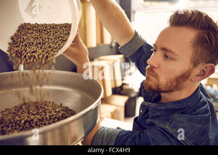 Man pouring grains de café dans une machine de torréfaction Banque D'Images