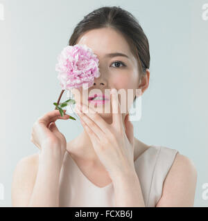 Femme avec le maquillage des lèvres roses tenant une fleur rose couvrant son œil de l'autre main sur son visage Banque D'Images