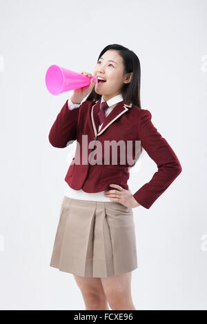 High school girl à l'uniforme scolaire parlant à travers un mégaphone en plastique avec sa main sur sa taille Banque D'Images