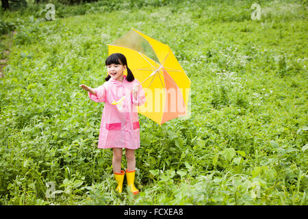 Jeune fille au manteau de pluie et des bottes de pluie parapluie jaune sous son bras s'étendant de l'avant dans le domaine Banque D'Images