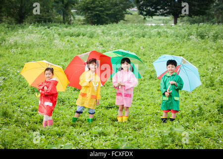 Quatre enfants en manteaux de pluie et des bottes de pluie dans un cadre permanent de chaque côté de l'autre sur le terrain avec un sourire Banque D'Images