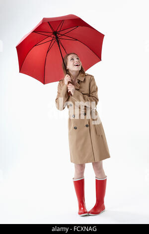 Young smiling woman wearing red parapluie, imperméable et bottes rouge standing looking up Banque D'Images