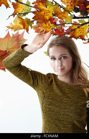 Portrait de jeune femme souriante avec de longs cheveux de toucher les feuilles d'automne stairng à l'avant Banque D'Images