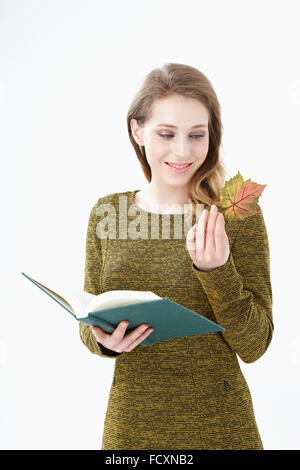 Portriat de young smiling woman holding un livre ouvert et une feuille tombée à la bas Banque D'Images