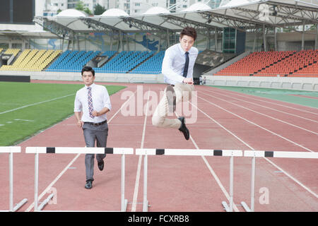 Hommes d'exécutant et sautant par-dessus des obstacles sur les voies à stade Banque D'Images