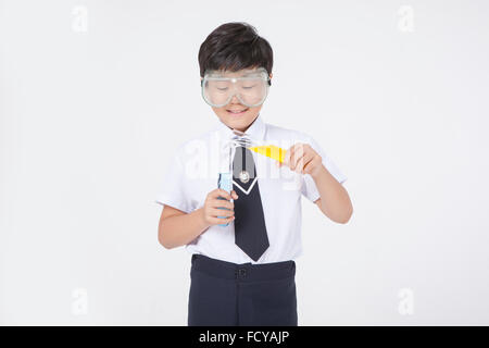 Garçon de l'école élémentaire en uniforme et lunettes de laboratoire faisant une expérience chimique Banque D'Images