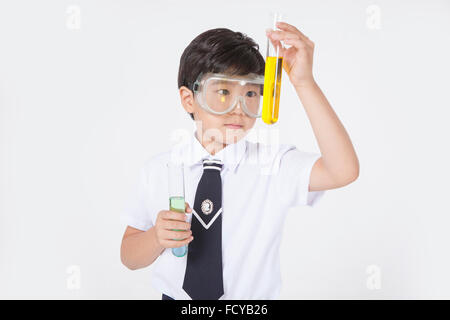 Garçon de l'école élémentaire en uniforme et lunettes de laboratoire faisant une expérience chimique Banque D'Images